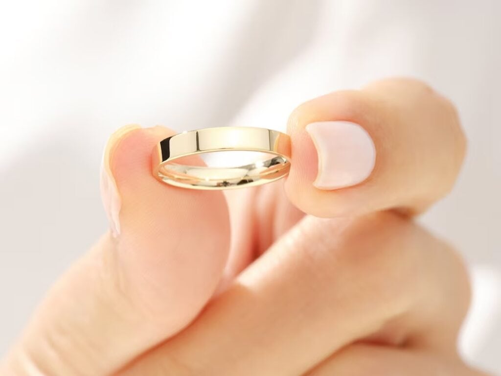 10k yellow gold flat wedding band in between fingers