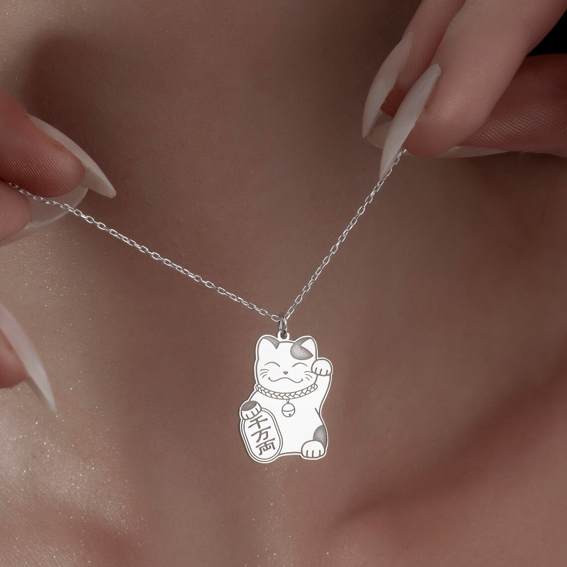 fingers holding maneki neko necklace